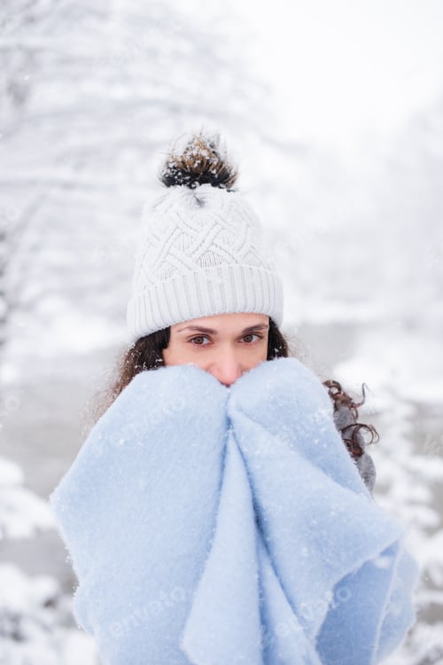 Preview: woman covering her face with scarf and wrapping herself in scarf walking in winter park