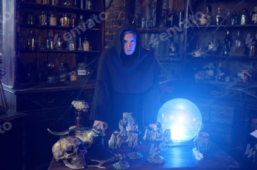 Preview: Male exorcist in hood near the magic crystal ball
