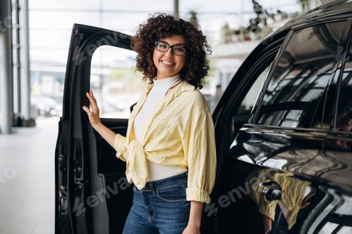 Preview: In jeans, white shirt, standing. Pretty woman is in the car retail shop