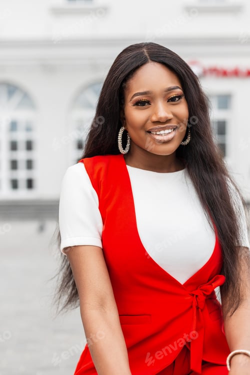 Preview: Fashionable positive young african woman with amazing smile in red stylish suit sitting and smiling