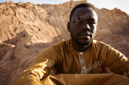 Preview: African American Man Sitting on Sand Dune in Desert in Sunlight