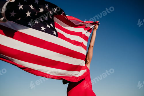 Preview: young woman holding a United States Flag over blue sky. 4th July in America concept