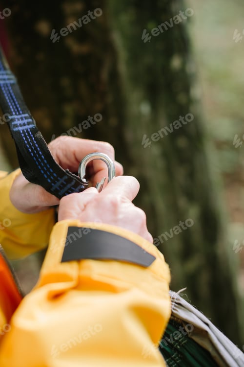 Preview: Person attaching hammock strap with metal carabiner in forest