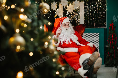 Preview: Santa claus relaxing in armchair with candy cane near christmas tree