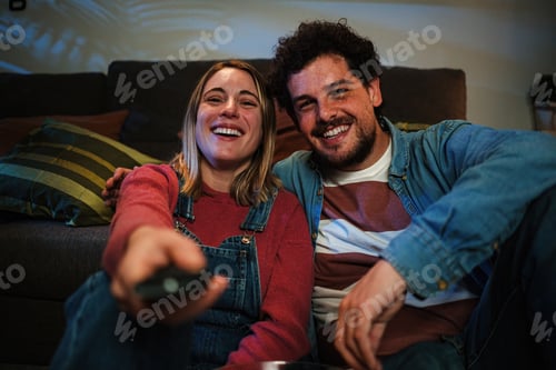 Preview: Front view of young caucasian couple smiling and having fun watching tv at late night sitting on the