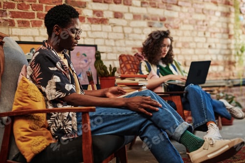 Preview: Young black man using smartphone sitting in armchair against his girlfriend