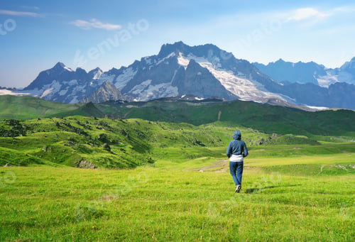 Preview: A woman looking on a green meadow, admiring the mountain scenery.