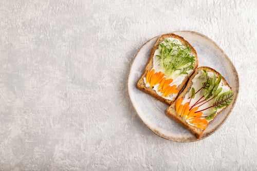 Preview: White bread sandwiches with cream cheese, calendula and microgreen on gray. top view, copy space.