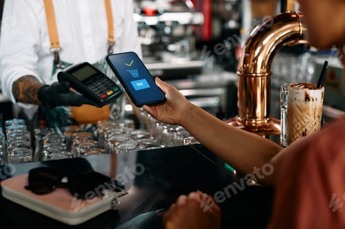 Preview: Close up of woman paying with smart phone at bar counter.