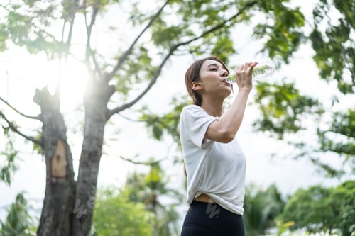 Preview: Asian young girl athlete drink bottle of water after exercise in park.