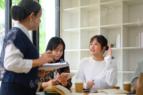 Preview: Pretty young woman student raising her hand to ask a question during class