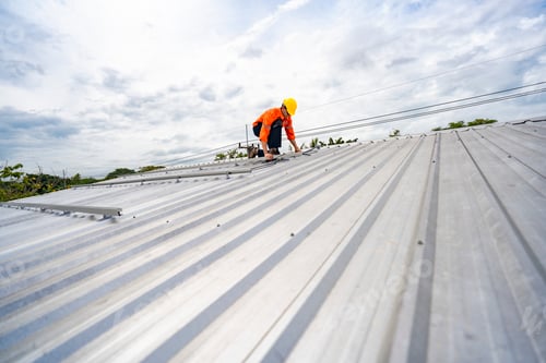 Preview: Technician in safety uniform and helmet kneeling on a rooftop