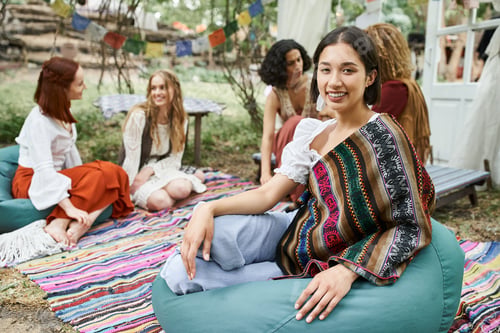 Preview: smiling young woman in boho outfit looking at camera near multiethnic friends in retreat center