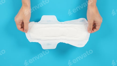 Preview: Hand is holding Sanitary napkin with wings for night use on blue background.