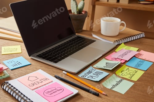 Preview: laptop with blank screen and paper stickers with business plan on tabletop