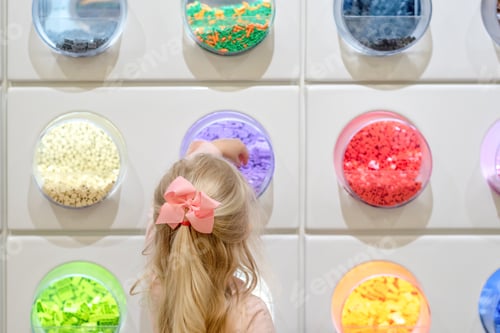 Preview: Little girl choosing plastic building blocks from brightly colored bins