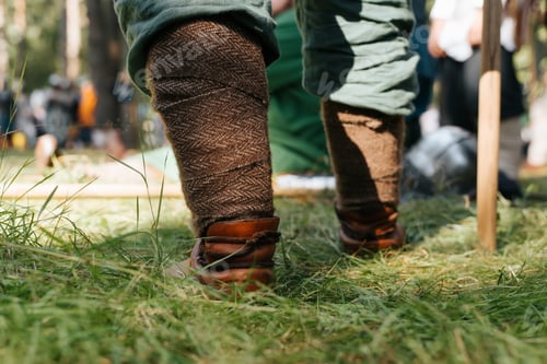 Preview: Close-up of a Viking leg in protective braid. Warrior standing on grass outdoors, low angle view.