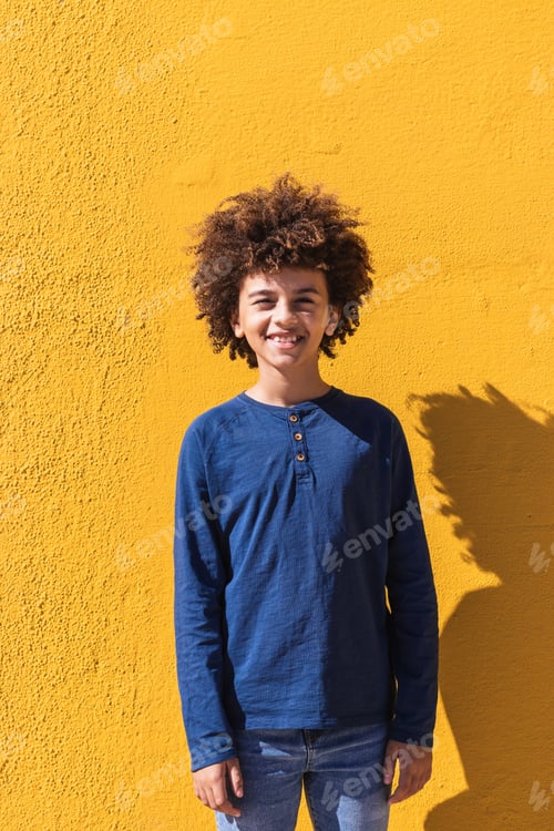 Preview: Ethnic boy with curly hair standing on yellow wall