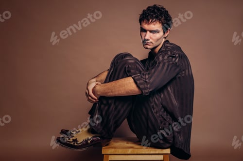 Preview: Young handsome man sitting on chair at studio