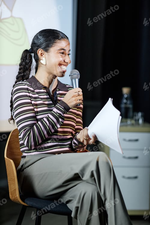 Preview: Young Adult Woman Smiling While Speaking into Microphone on Stage