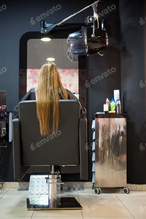 Preview: Rear view of woman sitting on hairdresser chair with long hair