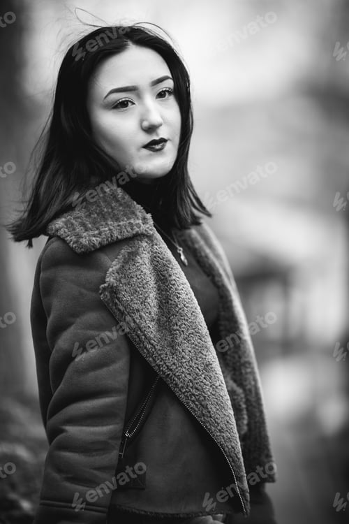Preview: Grayscale shot of a young Caucasian female wearing coat posing outdoors
