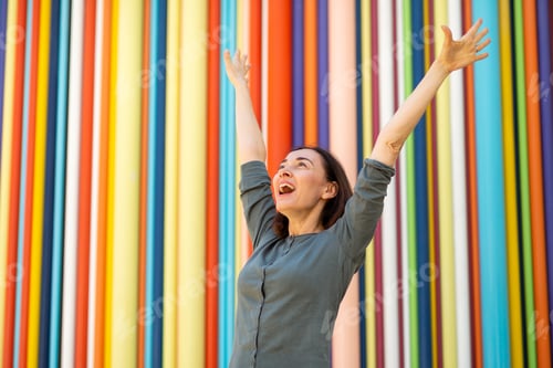Preview: happy woman against colorful background with arms in air