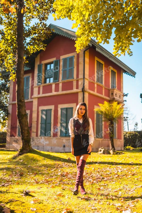 Preview: a young Caucasian brunette college girl, in a park next to a red house enjoying the fall
