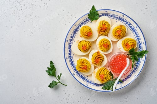 Preview: Stuffed eggs with red caviar and paprika on plate for appetizer easter table, top view, copy space.