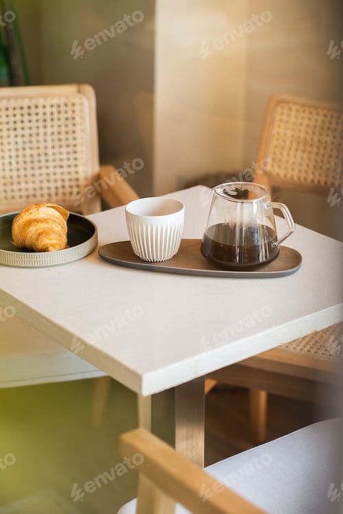 Preview: Vertical shot of a pour-over coffee in a glass jug with a white mug and croissant