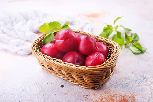 Fresh Plums in Woven Basket with Mint Leaves