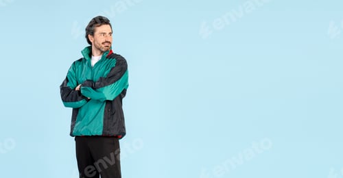 Preview: Confident sportsman looking away posing with crossed arms on blue background