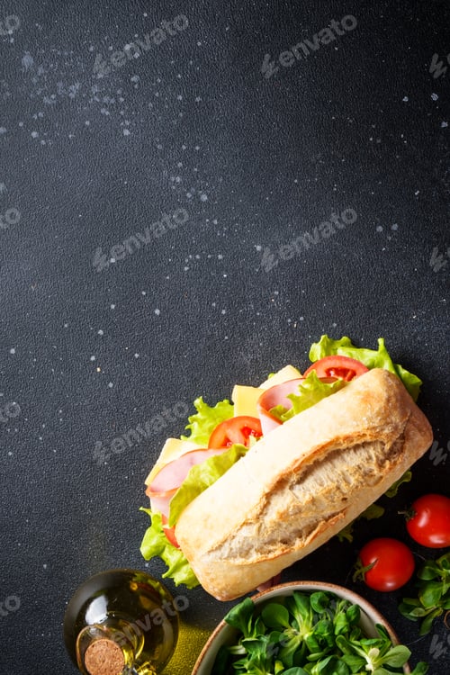 Preview: Ciabatta sandwich with lettuce, cheese, tomatoes and ham on black table.