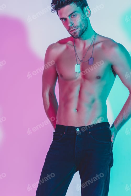 Preview: sexy, shirtless man in dark blue jeans holding hands behind back and looking at camera on background
