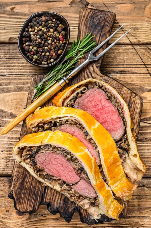 Preview: Sliced Beef Wellington pastry on a wooden cutting board. wooden background. Top view