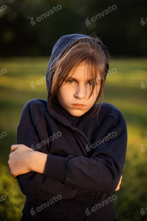 Preview: unhappy teenage girl with crossed hands walking in park in evening on green grass background