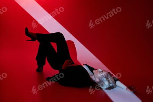 Preview: Woman lies on red background with ray of light on face. Sexy nude and confident
