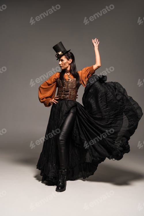 Preview: full length view of attractive steampunk woman in top hat with goggles standing with hand on hip on