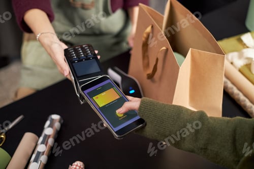 Preview: Caucasian Young Adult Woman Paying with Smartphone at Flower Shop Counter