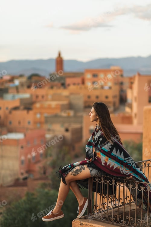 Preview: Woman sitting on roof terrace with aerial view of old arabian town Boumalne