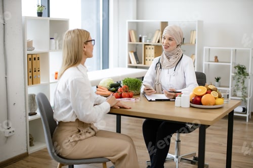 Preview: Muslim female doctor sitting at table writing diet plan talking with patient.