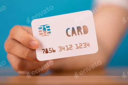Preview: Closeup shot of a person holding a credit card paper cut-out on a blue blurry background