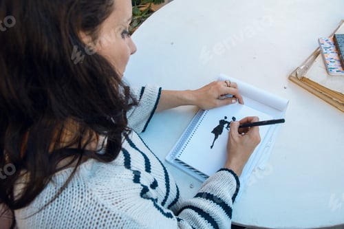 Preview: top view of woman at home sitting drawing on paper with black color marker, copy space.