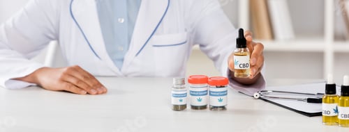 Visualização: vista recortada de médico afro-americano de jaleco branco segurando frasco com letras cbd na clínica,