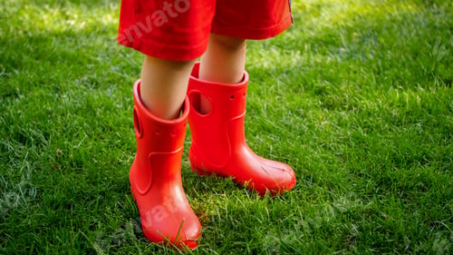 Preview: Closeup image of ittle boy in red rubber wellington boots standing on green grass lawn