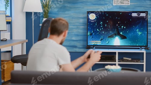 Preview: Man holding wireless controller playing console video game first person shooter on tv while sitting