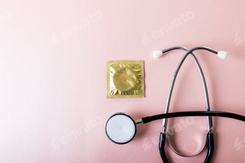 Preview: Directly above shot of stethoscope with condom in pack against pink background, copy space