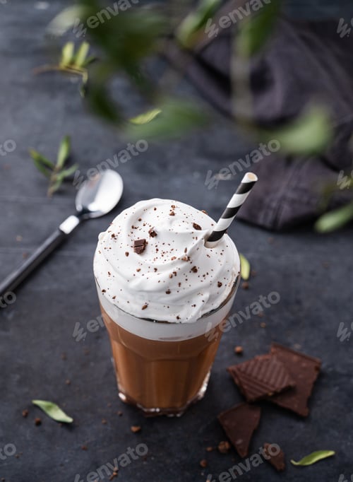 Preview: Hot chocolate with whipped cream and chocolate pieces in a glass on a dark background with a branch