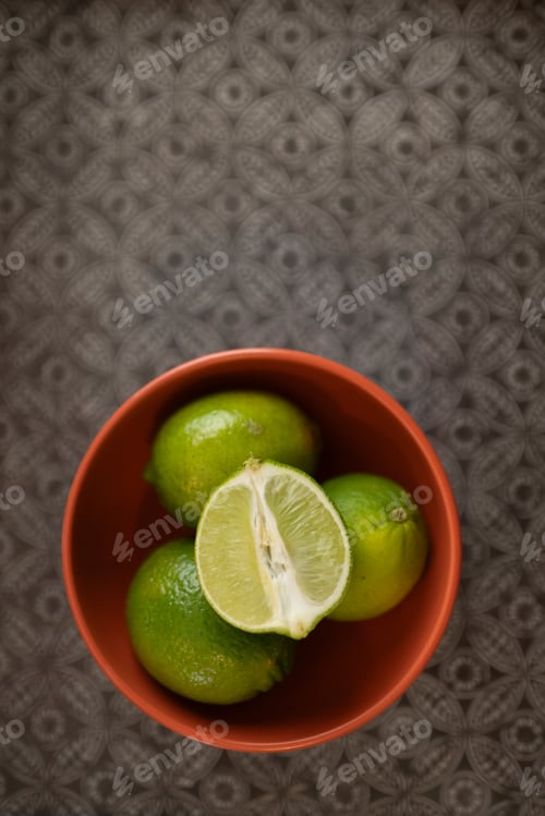 Preview: Top view of sliced limes in a modern orange bowl on a silver patterned tray