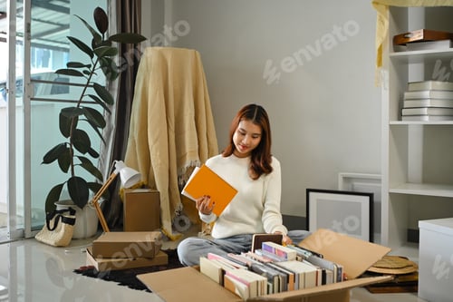 Preview: Smiling asian woman moving into new home, unpacking parcel box on floor in living room